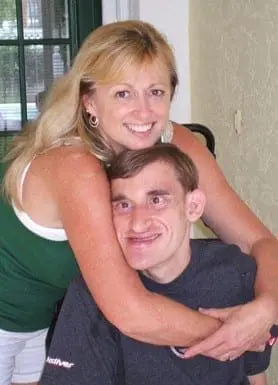 A woman hugs a man in a wheelchair, both smiling.