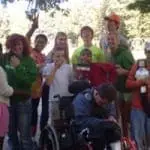 Group of happy children and young adults, some in a wheelchair, posing outdoors.