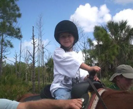 Young boy in riding helmet and white shirt on horseback.