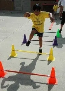 Young athlete hurdles over a low bar during a Special Olympics event.