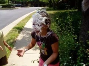 A person stands with their face covered in whipped cream and chocolate frosting.