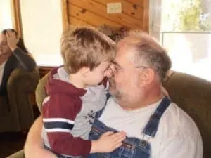 A man in overalls holds a young boy close, touching foreheads.