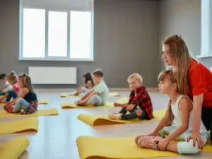 Instructor guiding children sitting on yoga mats in a bright studio.