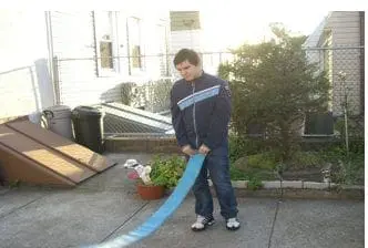 A young boy swings a blue exercise mat outdoors while staff supervise.