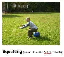 A person squats on a blue and white ball in a grassy field.