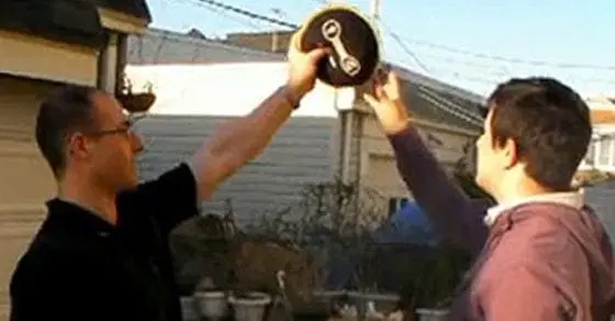 Two men hold up a round object with a circular symbol.