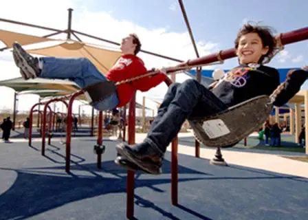 Two children laugh as they swing at Morgan's Wonderland, an accessible family fun park.