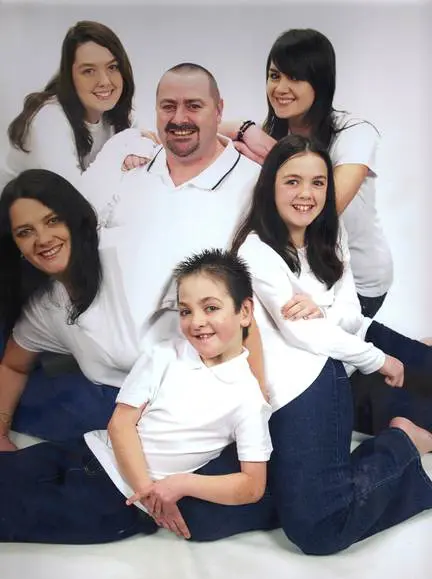 A family poses for a portrait, with a man and four children in white shirts and jeans.