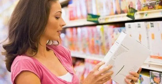 Woman reading the label of a product in a grocery store aisle.