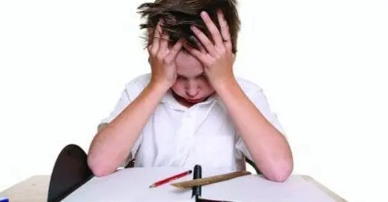 Child with head in hands at a desk with schoolwork.