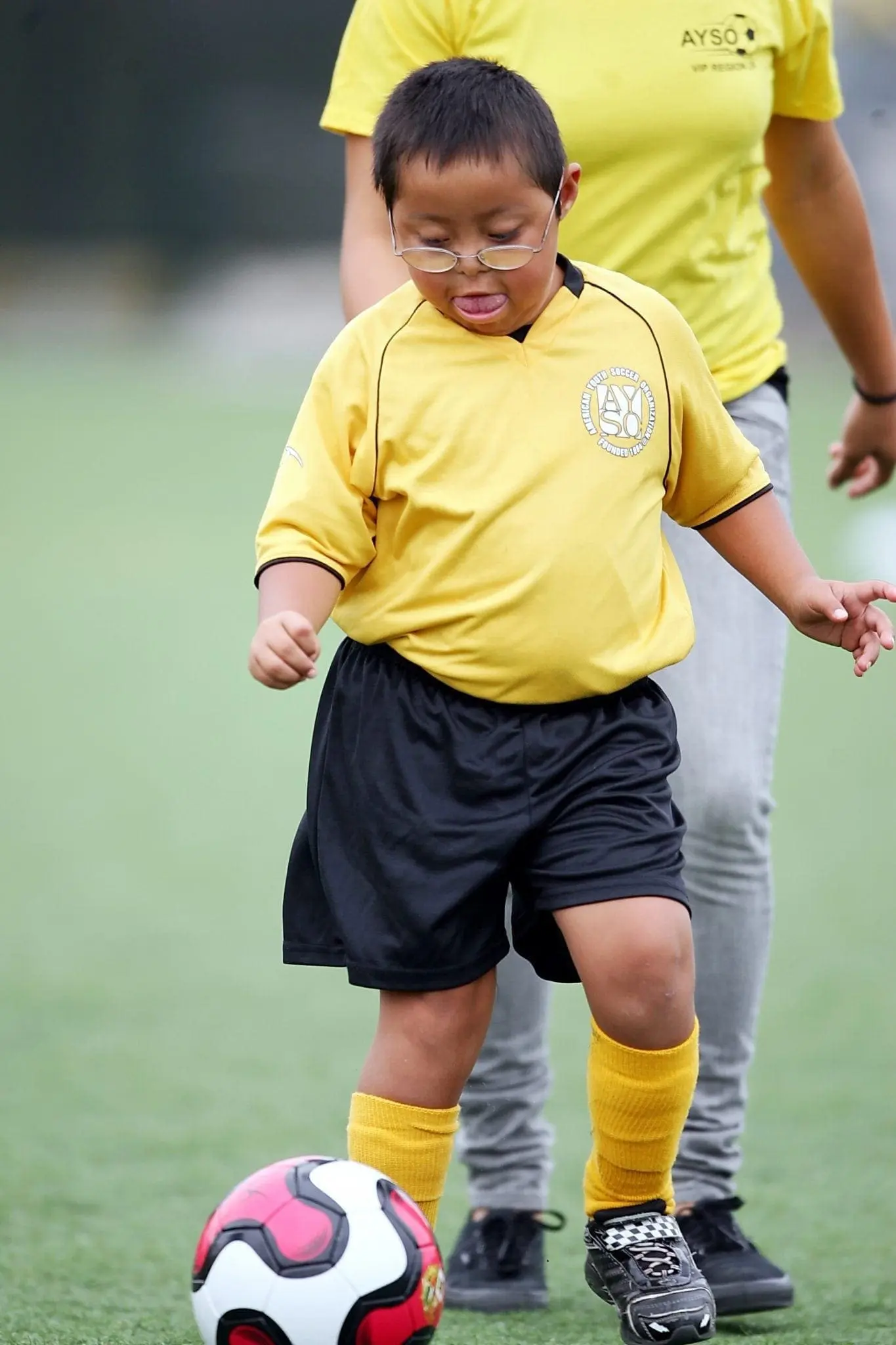 Boy in yellow AYSO uniform kicking a soccer ball.