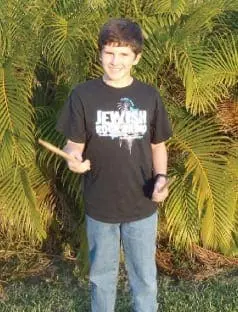 Evan smiles, holding drumsticks, wearing a black t-shirt with "Jewish Rock" on it.