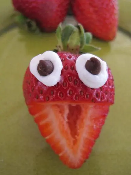 Strawberry decorated with frosting and chocolate chips to resemble a face.