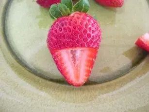 Strawberry cut in half horizontally, with green stem and part of another strawberry visible.