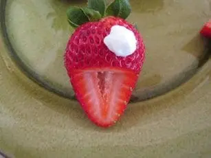 Strawberry with frosting and a chocolate chip eye on a plate