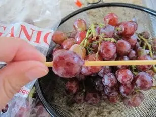 Hand threading frozen grapes onto a skewer for a caterpillar craft.