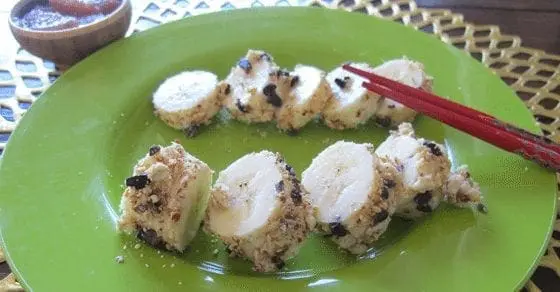 Banana sushi rolls coated in sprinkles on a green plate with chopsticks.
