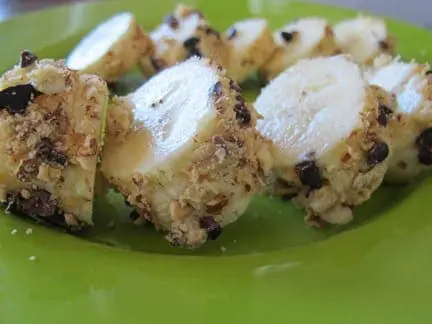 Banana pieces coated in crushed nuts and chocolate chips on a green plate.