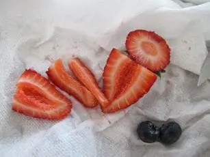 Sliced strawberries and two blueberries on a white paper towel.