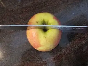 Knife cutting an apple in half on a counter.