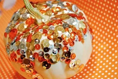 Small white pumpkin decorated with colorful sequins on an orange polka dot background.