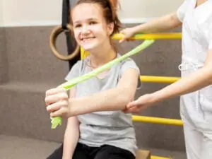 A smiling girl works with a physical therapist using a resistance band.