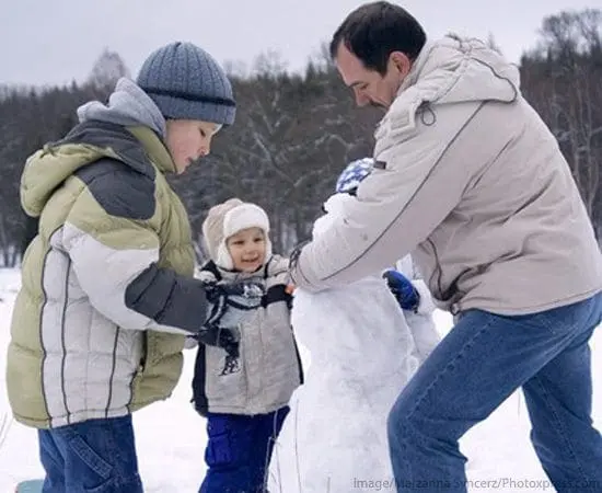 Man and two children building a snowman in the snow