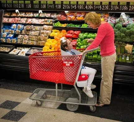 Woman pushing a shopping cart with a child in it through a grocery store aisle.