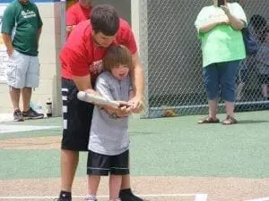 A young boy with his arm around a baseball bat held by a man.