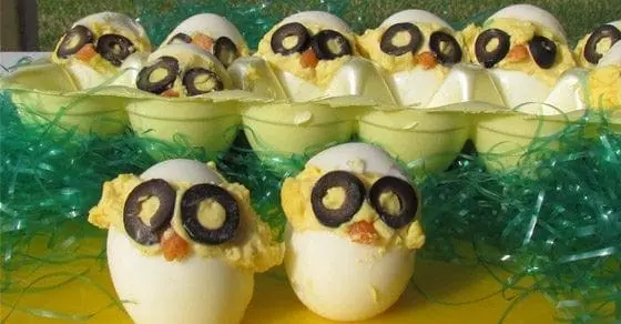 Deviled eggs decorated to look like chicks with olive eyes and carrot beaks.
