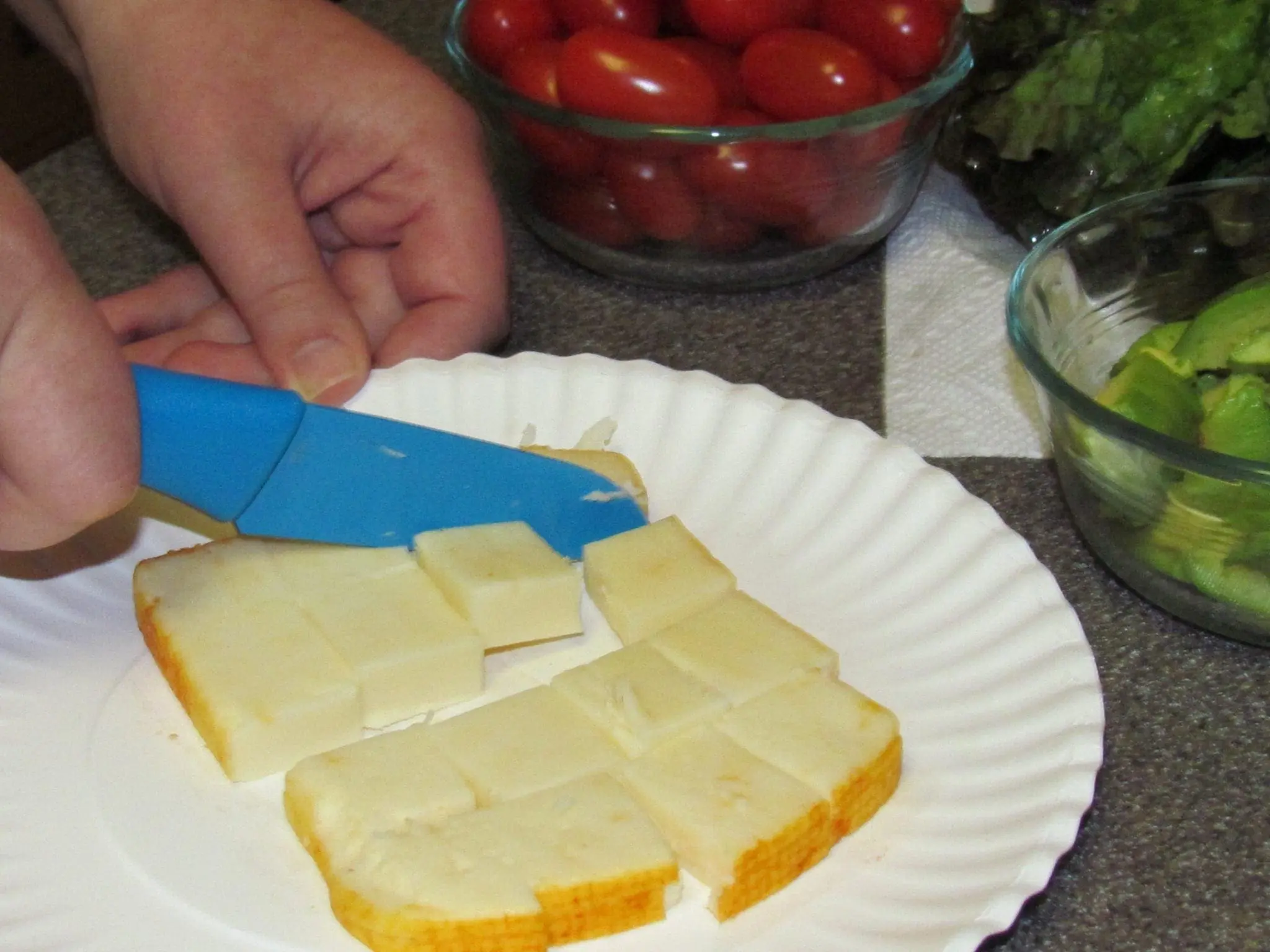 Hands cutting cheese into cubes on a paper plate.