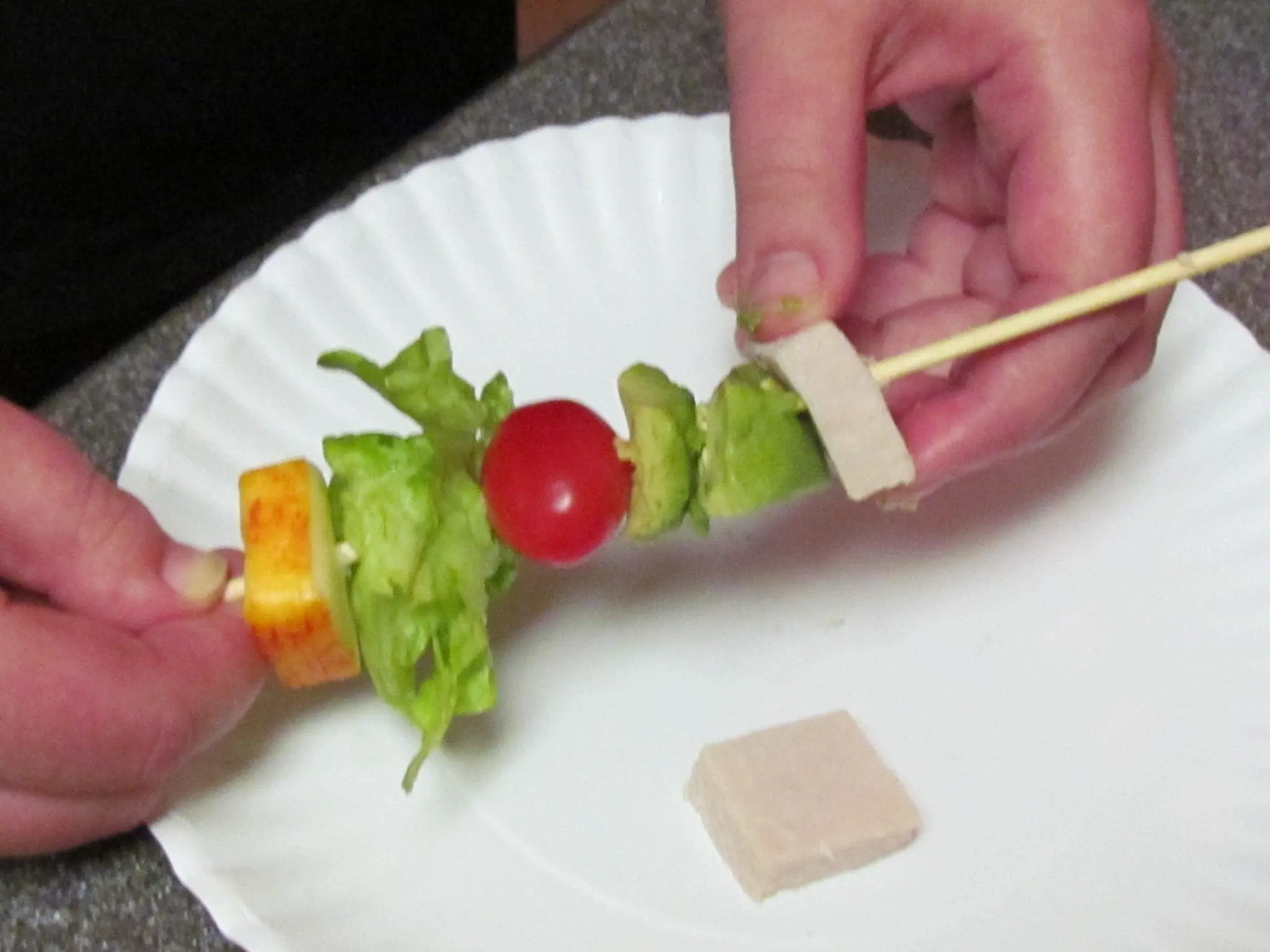 Assembling Kiddie Cobb on a Stick with cheese, lettuce, tomato, and avocado on a skewer.