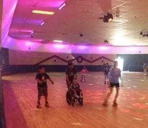 Children and adults on roller skates and in a wheelchair at a roller skating rink.