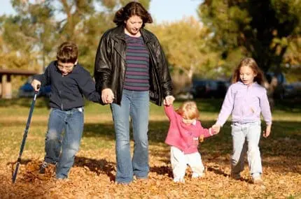 A mother walks outdoors holding hands with her three children.
