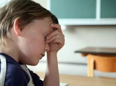 Young boy sitting at a desk with his hand on his forehead, looking frustrated and overwhelmed by learning challenges.