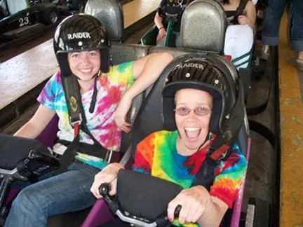 Two people wearing helmets sit in a race car, smiling.