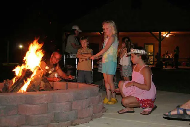 Families roast marshmallows over a bonfire at night.