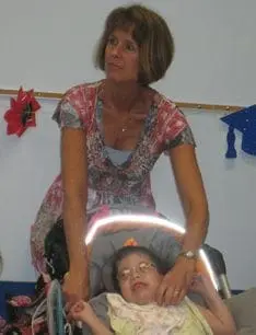 Patricia Biagioli smiles while assisting a young girl in a wheelchair.