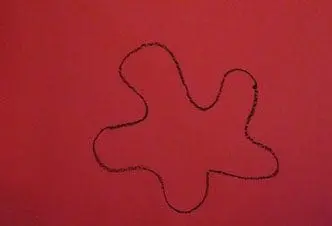 A black crayon drawing of a blob shape on red paper.