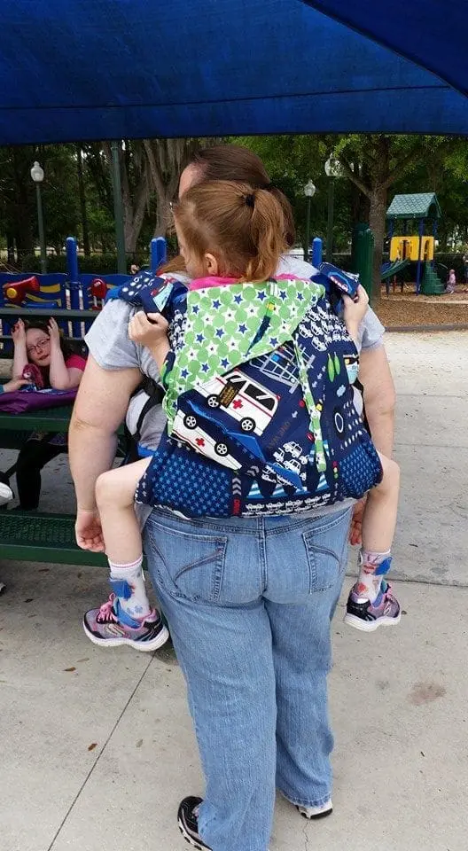Woman carrying a child in a decorated backpack carrier.