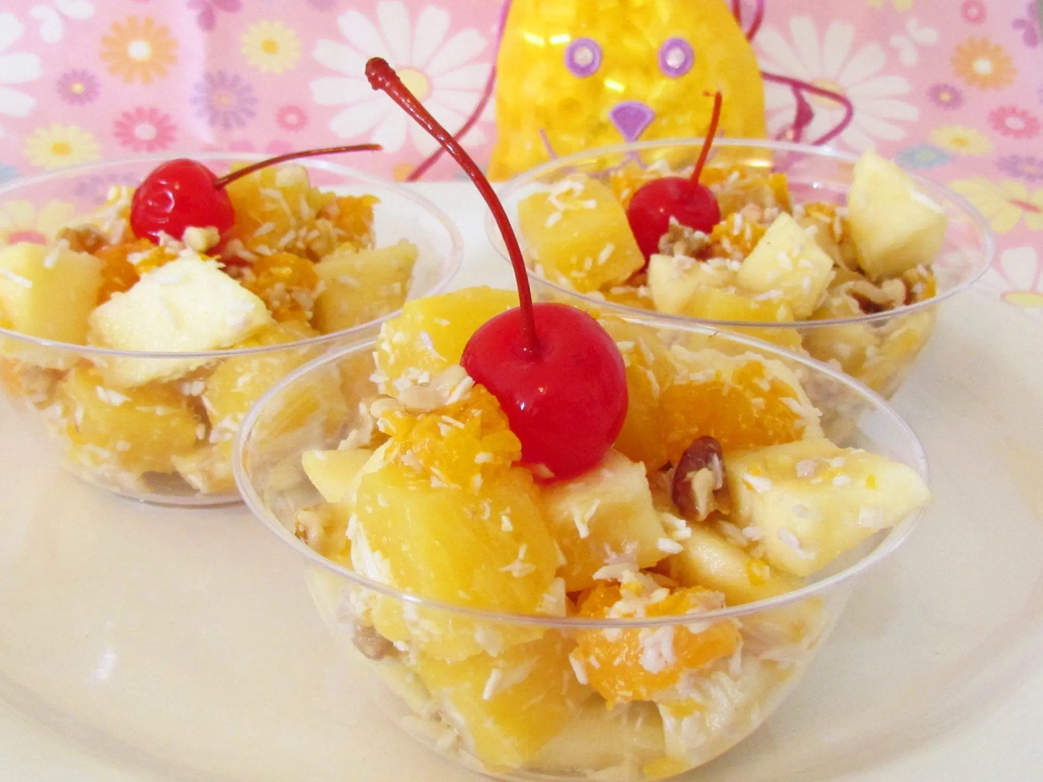 Ambrosia fruit salad in clear cups topped with cherries.
