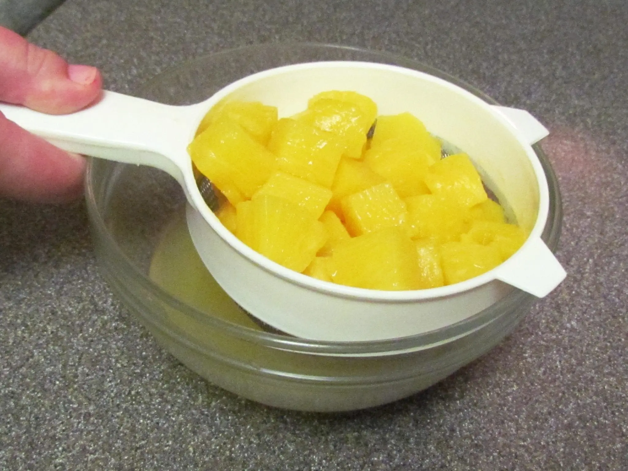 Draining pineapple chunks in a strainer over a glass bowl.