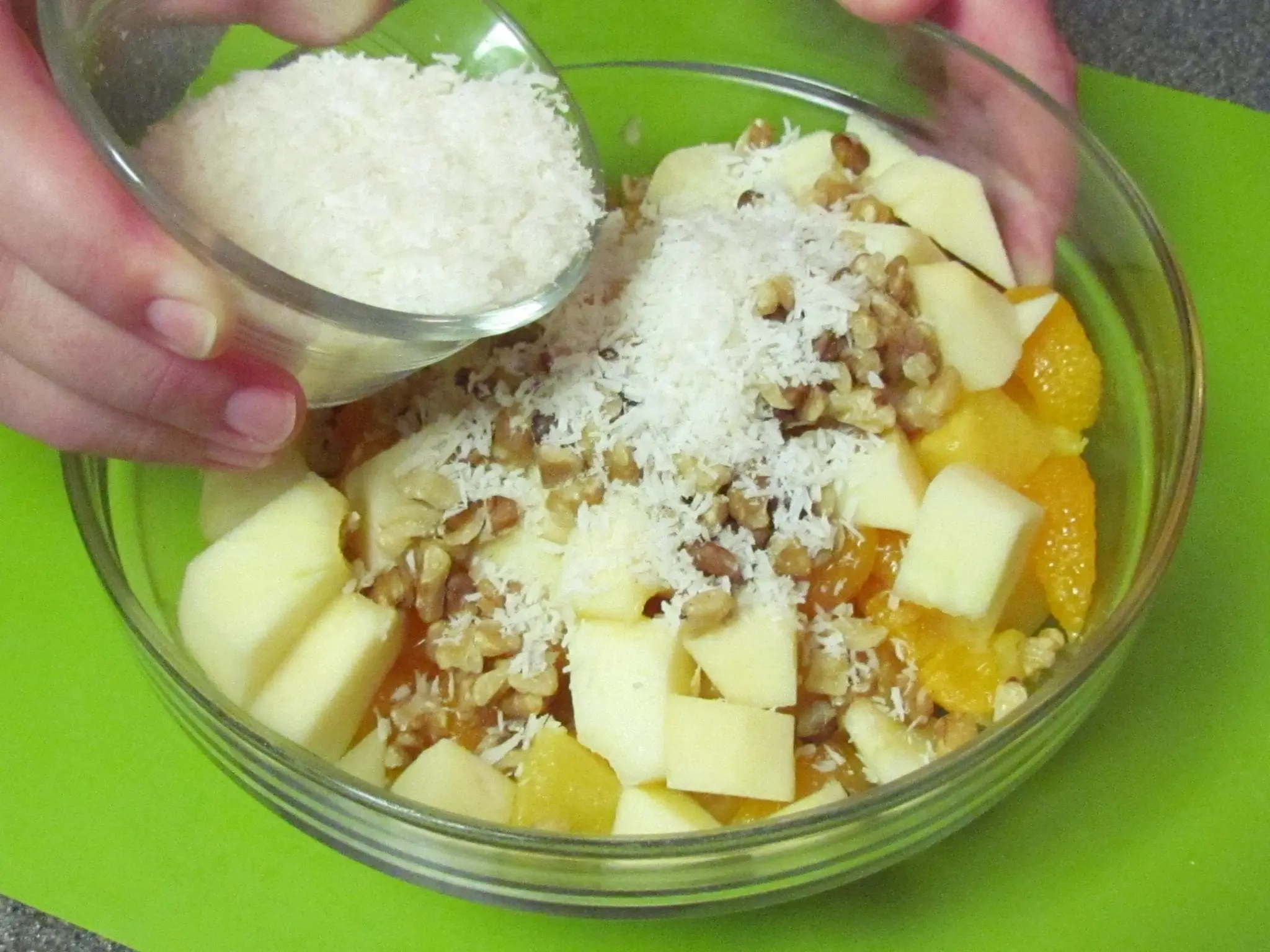 Shredded coconut is added to a bowl of fruit and nuts for ambrosia salad.