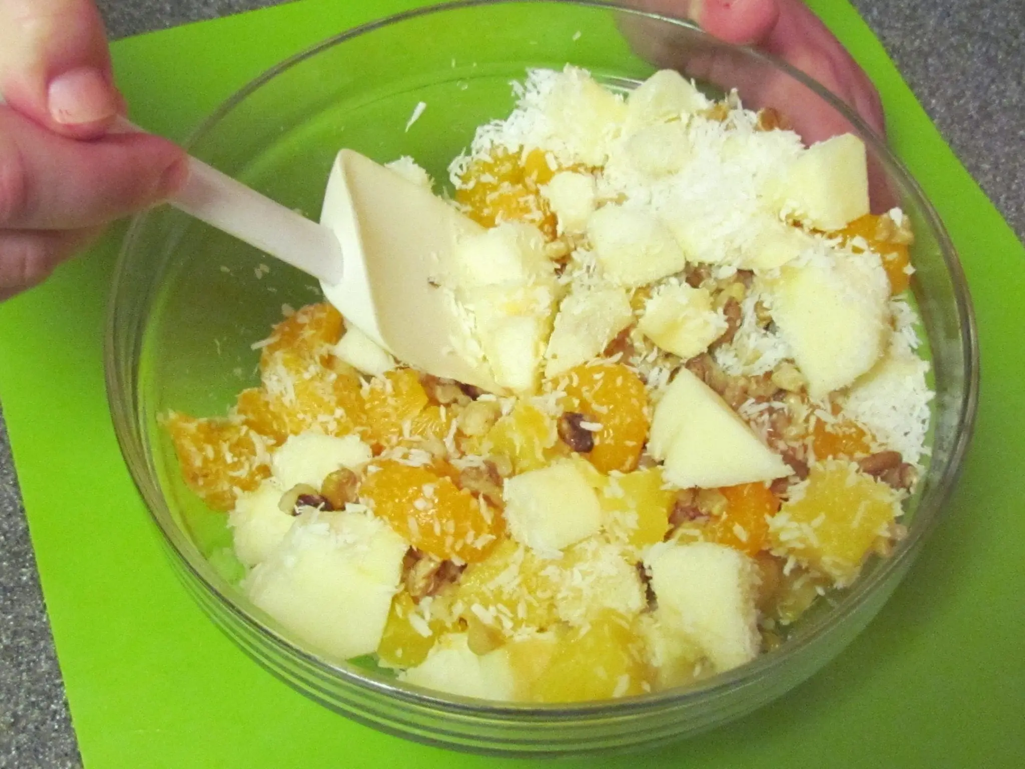 Mixing fruit salad ingredients in a clear bowl.