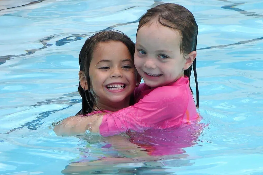 Two smiling children hugging in a swimming pool.