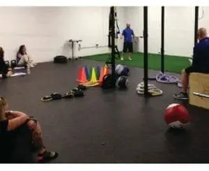 People in a gym with exercise equipment and cones for training.