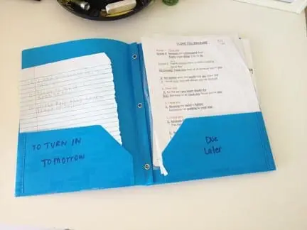 Blue folder with labeled pockets holding school papers for organization.