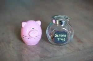 A pink pig timer and a glass jar labeled "Screen Time" sit on a wooden surface.