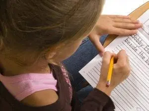 Young child writing on a worksheet with a pencil.
