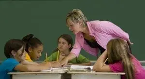 Teacher helps students at desks in a classroom.
